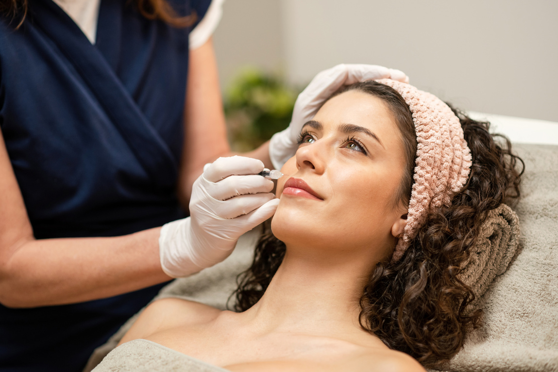 Anonymous beautician injecting filler into lips of female client